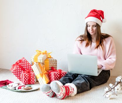 Christmas planing, online shopping concept. Young woman in santa hat shopping online surrounded by presents