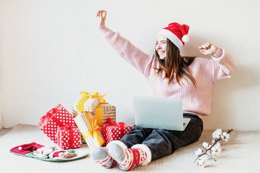 Christmas planing, online shopping concept. Young woman in santa hat shopping online surrounded by presents