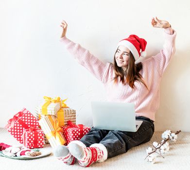 Christmas planing, online shopping concept. Young woman in santa hat shopping online surrounded by presents