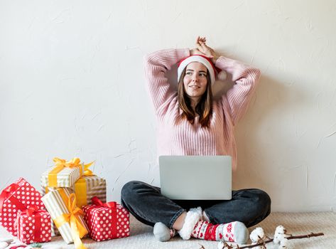 Christmas planing, online shopping concept. Young woman in santa hat shopping online surrounded by presents