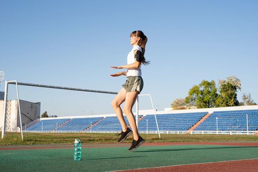 Healthy lifestyle concept. Teenager girl working out at the stadium doing high knees exercise