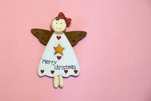 wooden angel with inscription on merry christmas dress on pink background, copy space.