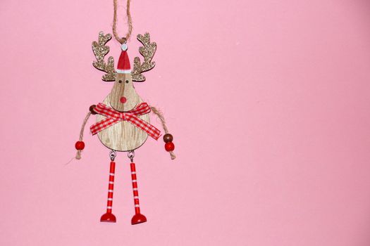 wooden deer with golden shiny antlers in santa hat on pink background, copy space.