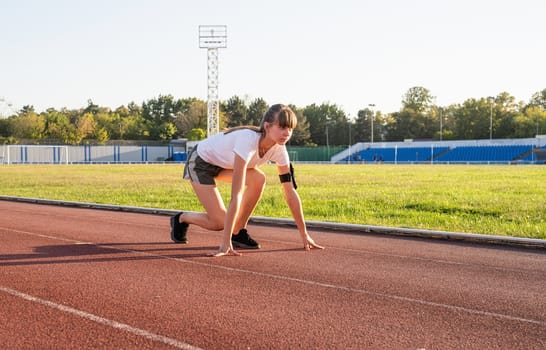 Sports and fitness. Teenager girl getting ready to run at stadium track