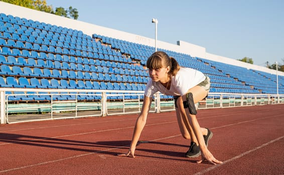 Sports and fitness. Teenager girl getting ready to run at stadium track