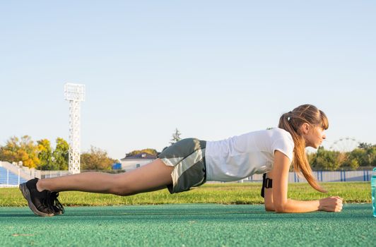 Teenager girl doing workout standing in a plank position at the stadium