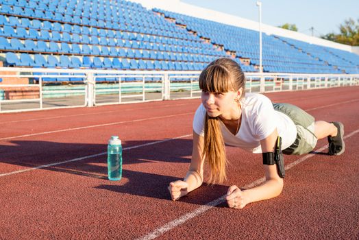 Teenager girl doing workout standing in a plank position at the stadium