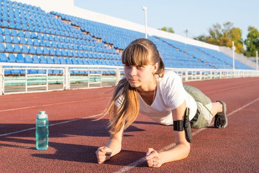 Teenager girl doing workout standing in a plank position at the stadium