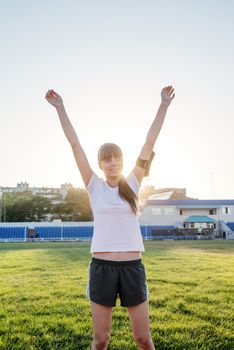 Teenager girl standing on the track rising her arms