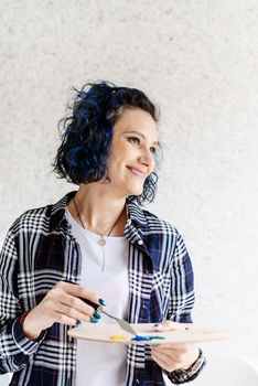 Portrait of smiling woman artist putting oil paints on palette working in her studio