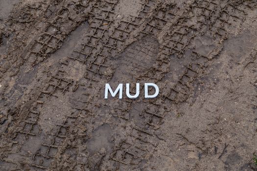 the word mud laid with silver metal letters on wet dirt surface with directly above perspective under cloudy autumn day light