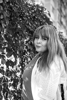 Portrait of a young beautiful caucasian plus size woman standing on the street next to the wall smiling, black and white