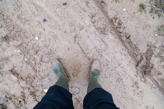 feet in green rubber boots stands on wet brown mud directly above view, directly above first person gonzo view
