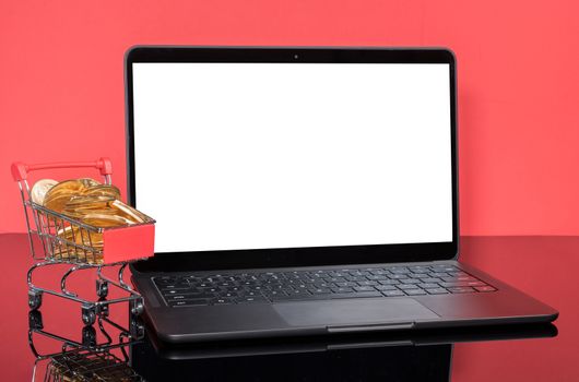Concept for online and winter sales with shopping cart filled with gold coins in front of a modern laptop computer with isolated screen