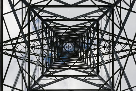 Dark abstract image of the inside of an electrical pylon. Interior skyward view, looking up, lattice structure creates an industrial themed pattern.
