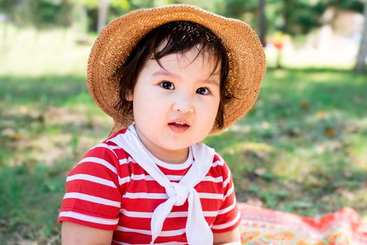 Parks and recreation. Cute asian infant girl in a stripped red dress and srtaw hat on a picnic in the park