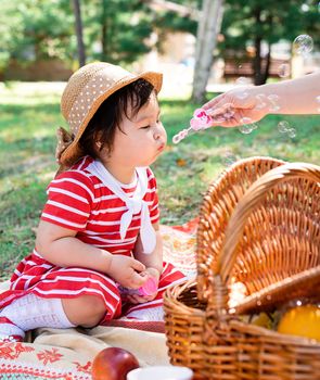 Parks and recreation. Cute asian infant girl in a stripped red dress and srtaw hat on a picnic in the park