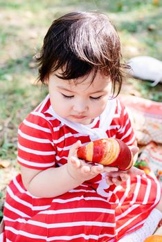 Parks and recreation. Cute asian infant girl in a stripped red dress and srtaw hat on a picnic in the park