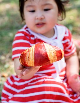 Parks and recreation. Cute asian infant girl in a stripped red dress and srtaw hat on a picnic in the park