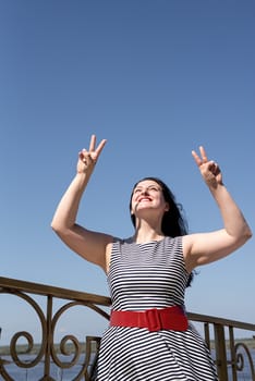 Happiness concept. Beautiful young woman opened her hands at the blue sky showing peace gesture