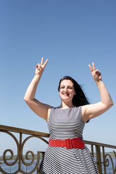Happiness concept. Beautiful young woman opened her hands at the blue sky showing peace gesture