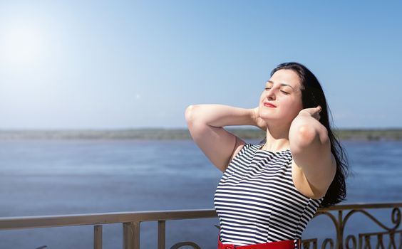 beautiful young woman standing by the riverside enjoying the view in the summer day