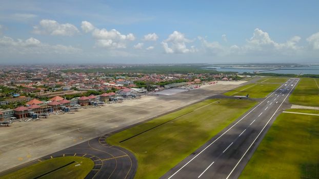 Airport - aerial view with runways, taxis, grass and air-crafts. Aerial view to Ngurah Rai airport. The plane goes down the runway.