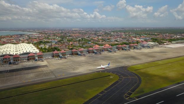 Airport - aerial view with runways, taxis, grass and air-crafts. Aerial view to Ngurah Rai airport. The plane goes down the runway.