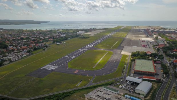 A view of Bali island after aircraft has been taken off from Ngurah Rai International airport. Runway reaching into the ocean. Aerial view to international airport in Denpasar.