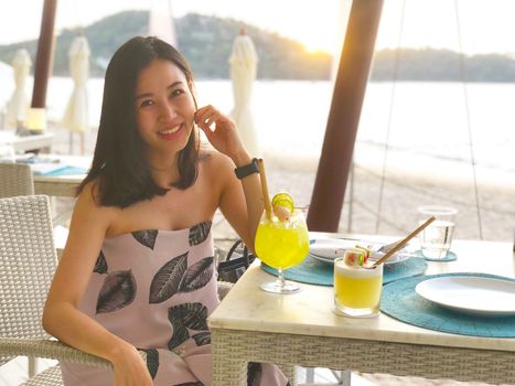 Beautiful woman holding a fruit cocktail on a tropical beach at sunset 