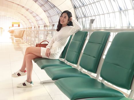 Young woman smiling with green chair sitting in airport hall while waiting landing