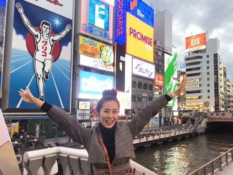 Osaka,Japan - Mar 26, 2019 : A young tourist woman tried to take the same pose as the Glico man neon signboard which is one of the most famous landmark Dontonbori in Namba Osaka,Japan. 