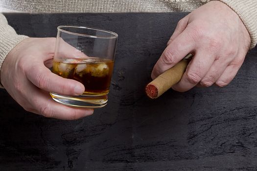 Men's hands with a cigar and a glass of whiskey