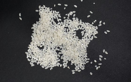 Scattered white uncooked rice on a black background