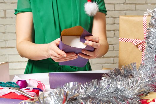 Woman wrapping christmas presents to violet packing paper. woman hands packing a christmas gift, diy gift packing and wrapping concept.