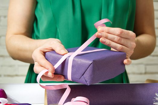 Woman wrapping christmas presents to violet packing paper. woman hands packing a christmas gift, diy gift packing and wrapping concept.