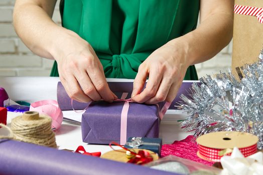 Woman wrapping christmas presents to violet packing paper. woman hands packing a christmas gift, diy gift packing and wrapping concept.