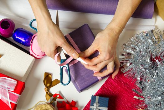 Woman wrapping christmas presents to violet packing paper. woman hands packing a christmas gift, diy gift packing and wrapping concept.