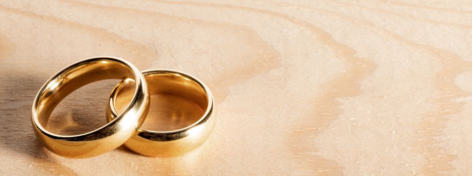 Two golden wedding rings on wooden background with copy space for text