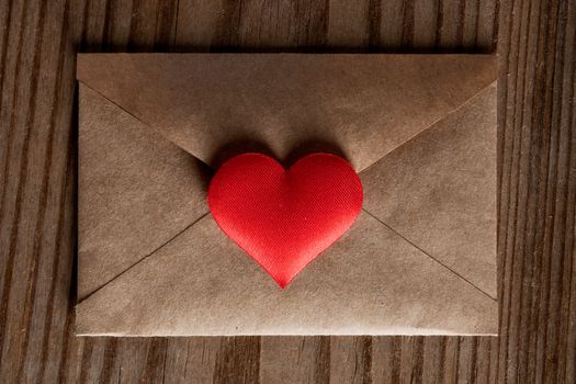 Valentine day love letter, envelope of craft paper with red heart on wooden background