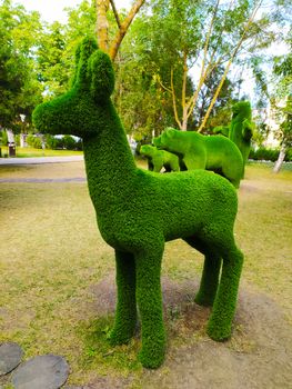 Sculpture of a deer in profile in a green Park against a background of trees.