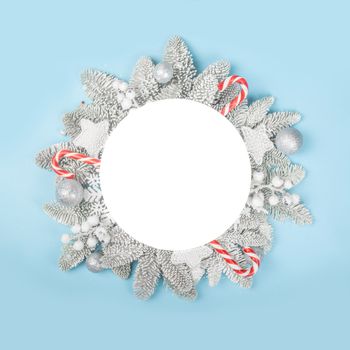 Frosted fir tree twigs and Christmas decorative bauble balls on blue background with white circle card with copy space for text template flat lay top view design