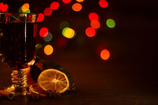 Mulled wine with cinnamon sticks and orange over holiday christmas lights background