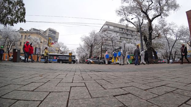 Trees covered with snow, urban environment. Street for walking, people go about their business, cars pass on the road, children ride on a swing. Snow-white trees, Christmas mood. Almaty, Kazakhstan.