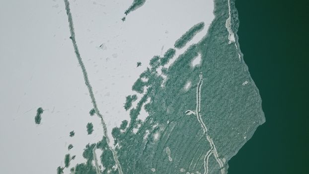 The boundary between the ice and the lake. The view from the top. Green water and white ice. Big lake Balkhash in Kazakhstan. Early spring. Ice breaks are visible, and white snow lies in places.