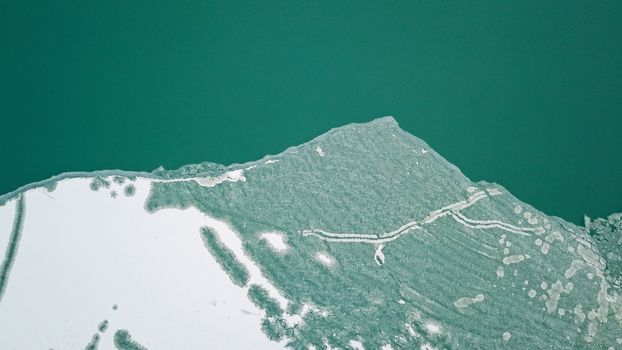 The boundary between the ice and the lake. The view from the top. Green water and white ice. Big lake Balkhash in Kazakhstan. Early spring. Ice breaks are visible, and white snow lies in places.