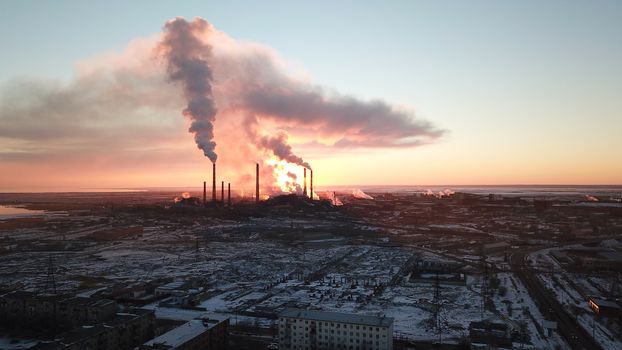 Epic sunset on the background of a Smoking factory. The red sun with bright rays goes beyond the pipe factories and smog. Shooting with the drone. View of part of the city, lake and industry. Red sky