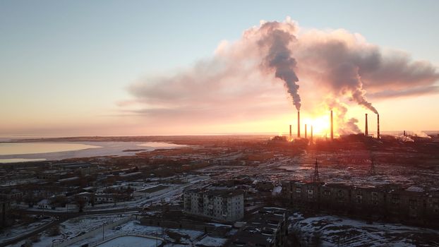 Epic sunset on the background of a Smoking factory. The red sun with bright rays goes beyond the pipe factories and smog. Shooting with the drone. View of part of the city, lake and industry. Red sky