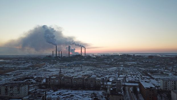 Epic sunset on the background of a Smoking factory. The red sun with bright rays goes beyond the pipe factories and smog. Shooting with the drone. View of part of the city, lake and industry. Red sky