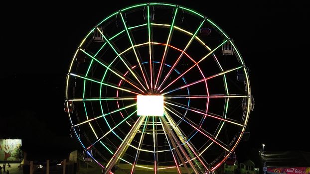 The observation wheel shimmers with different colors. Night. It is completely dark, but the Ferris wheel glows brightly. People relax, go for a walk. Kok-Tobe, Almaty. Like a festival.